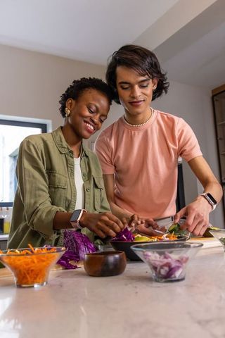 Diverse young couple preparing colorful salad together in bright home kitchen