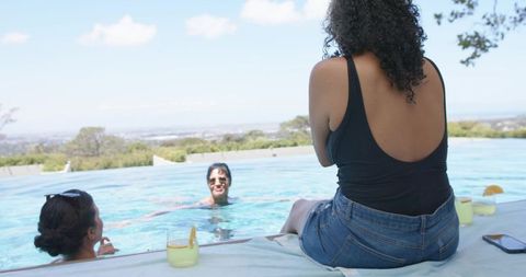 Poolside friends relaxing with cocktails and smartphone overlay over infinity pool horizon