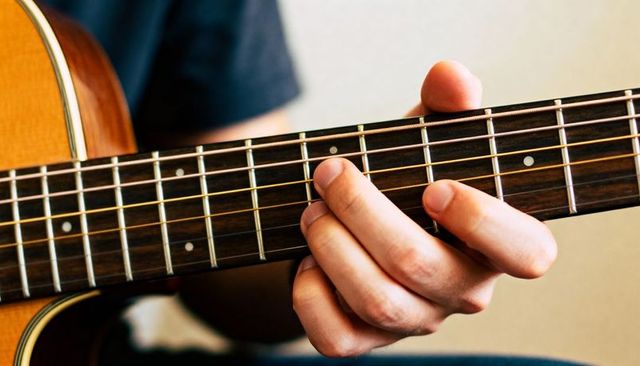 Fretting hand pressing chord on acoustic guitar fretboard close-up warm woodgrain