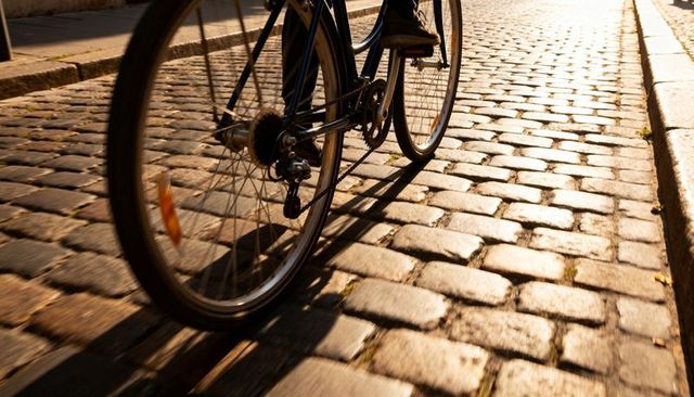 Sunlit bicycle rolling on historic cobblestone street, close-up rear wheel and drivetrain