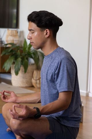 African american man meditating at home on blue yoga mat wearing smartwatch and casual activewear