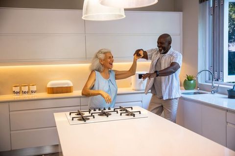 Senior couple dancing in modern kitchen with labeled canisters