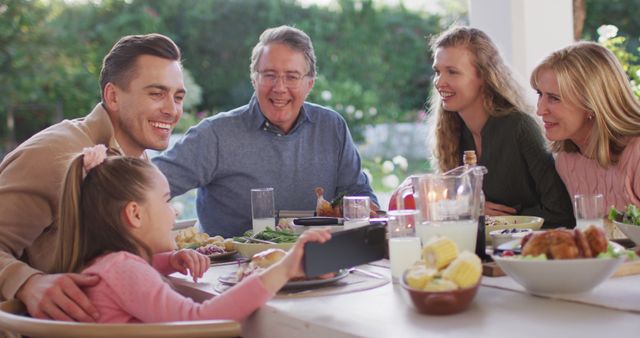 Image of happy caucasian parents, daughter and grandparents at dinner table looking at smartphone. Family, domestic life and togetherness concept digitally generated image.