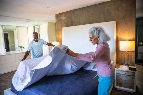 Senior couple making bed in modern minimalist bedroom setting