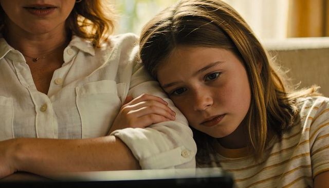 Child leaning on mother while watching laptop, sharing quiet comforting family moment