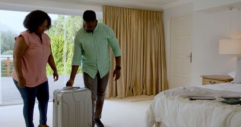 Joyful Couple Planning Vacation Together with Luggage in Bedroom