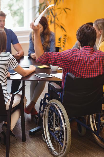 Business professionals in a meeting room discussing ideas. One individual in a wheelchair is actively participating, symbolizing diversity and inclusiveness. Perfect for illustrating inclusive workplaces, professional collaboration, team dynamics, and corporate environments.