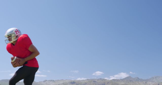 Football player in red jersey running with ball on field with mountains in background - Download Free Stock Images Pikwizard.com