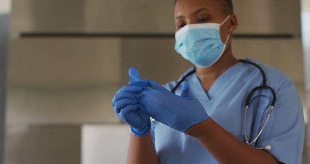 Healthcare professional wearing scrubs, stethoscope, and face mask, putting on protective gloves. Ideal for content related to healthcare, medical safety, patient care, nurse and doctor duties, or health industry promotions, particularly focusing on hygiene and protection protocols.