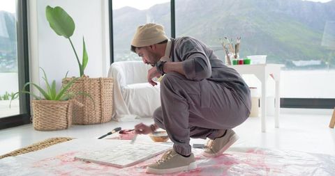 Indian artist painting on floor in minimalist sunlit studio, creative process, mountain view