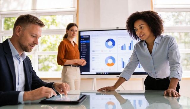 Team Collaborating Over Analytics Dashboard While Colleague Using Tablet in Bright Office