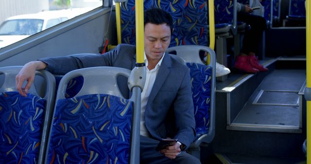 Businessman in suit traveling on public bus and using smartphone. Ideal for representing topics related to commuting, urban transportation, productivity while traveling, work-life balance, and modern corporate lifestyle.