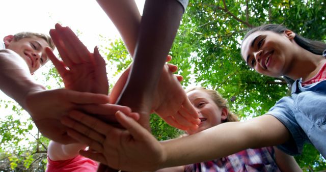 A group of young, diverse children are stacking their hands together in a gesture of teamwork and unity, with copy space. Their smiling faces suggest a sense of accomplishment and camaraderie.