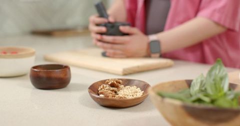 Grinding herbs and nuts with mortar and pestle in home kitchen with wooden bowls