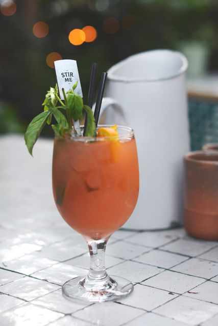Refreshing iced cocktail served in a wine glass garnished with fresh basil leaves and an orange slice. Perfect for summer outdoor parties, cocktail menus, or bar advertisements.