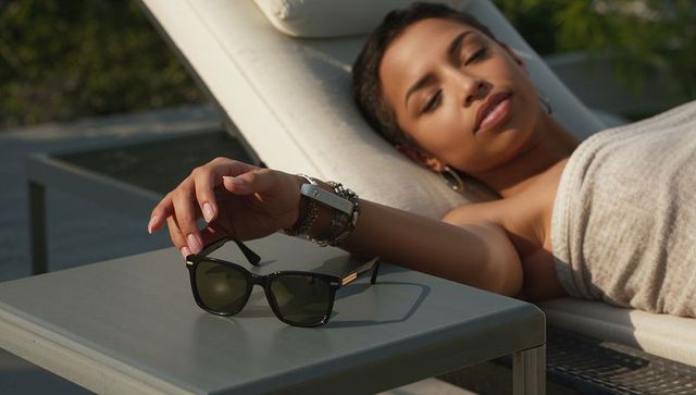 Reclining black woman relaxing on lounge chair reaching for sunglasses on sunny patio