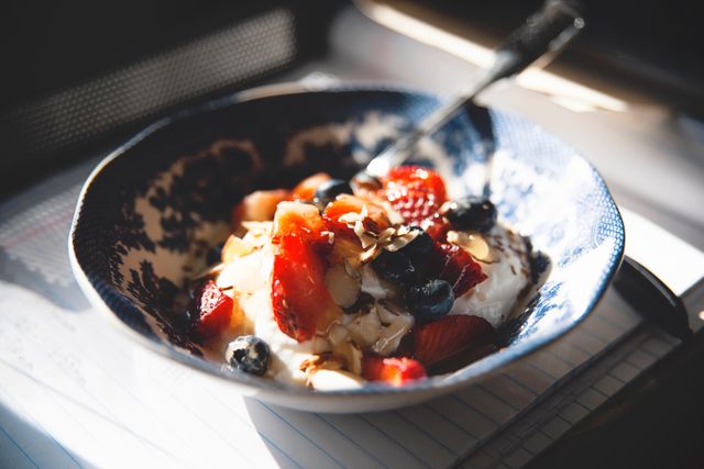 Bowl of Greek yogurt topped with fresh strawberries, blueberries, and sliced almonds. This nutritious, colorful breakfast option is perfect for promoting healthy eating habits. Suitable for food blogs, nutrition articles, and healthy recipe content.