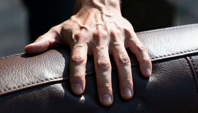 Male hand pressing brown leather car seat showing veins, fingers, seam and stitching