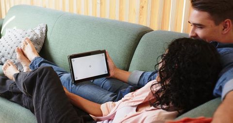 Diverse Couple Relaxing on Green Sofa Sharing Tablet in Bright Minimalist Living Room