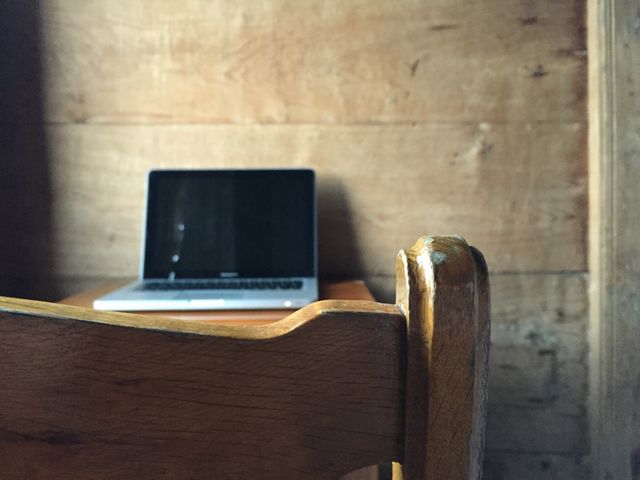 Laptop placed on wooden desk. Cozy and rustic atmosphere created by wooden backdrop and desk. Ideal for illustrating remote work environments, minimalist interior design, or homely office setups. Suitable for promoting cozy interiors, freelance work, or home office products.