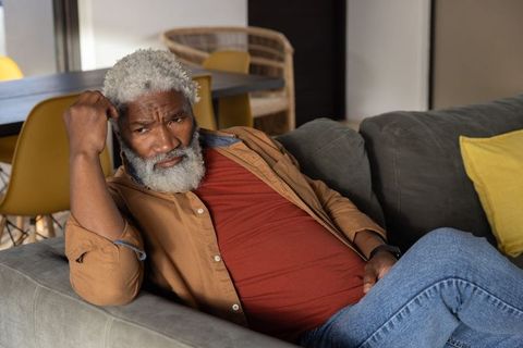 Senior african american man reclining on sofa looking contemplative in cozy living room