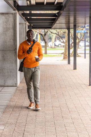 Commuter walking with coffee and phone under modern canopy on city campus walkway