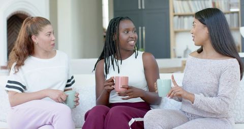 Diverse friends chatting over coffee on bright living room sofa