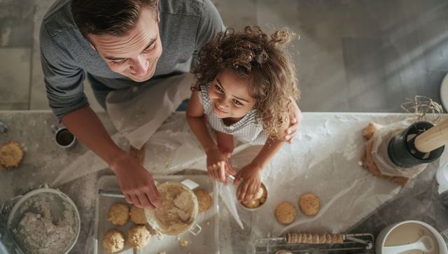 Dad and daughter baking cookies in sunlit kitchen, overhead view, flour-covered counter