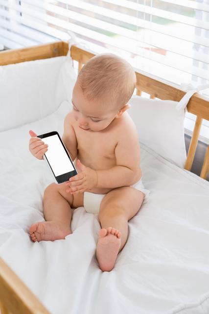 Baby boy playing with mobile phone on a cradle at home