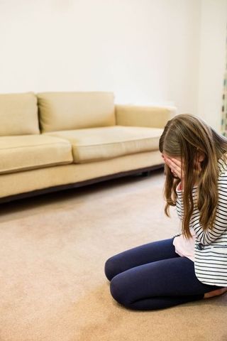School-age Girl Overwhelmed Emotion Kneeling on Carpet in Living Room
