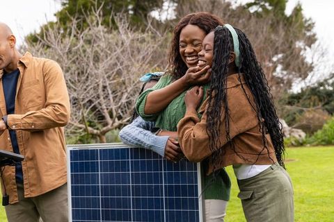 African american family hugging over solar panel in backyard celebrating clean energy now
