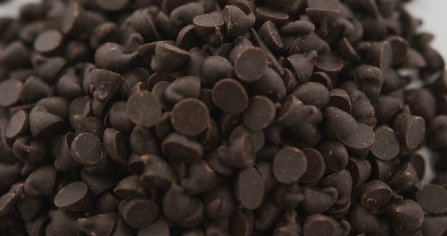 Macro shot of dark chocolate chips showcasing texture and richness. Ideal for content related to baking recipes, dessert preparations, food blogs, or culinary tutorials. Highlights purity of chocolate, suitable for advertisements or packaging designs.