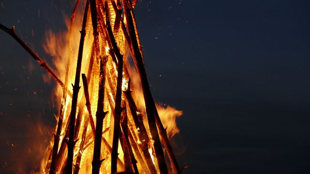 Large bonfire made of stacked logs burning against a dark night sky. Ideal for imagery related to outdoor events, camping, warmth, survival skills, celebratory bonfires, and night gatherings.