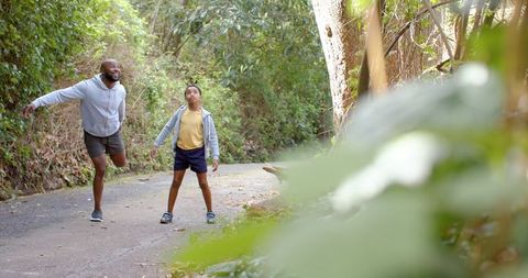 African american dad and son balancing on forest trail enjoying outdoor fitness bonding