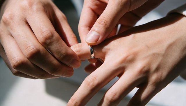 Placing polished wedding band onto partner finger closeup intimate commitment moment