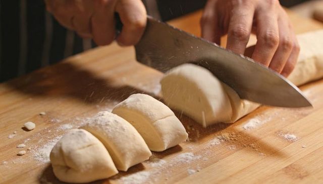 Slicing Dough Log with Chef Knife on Wooden Board for Rustic Bakery Pastry Prep