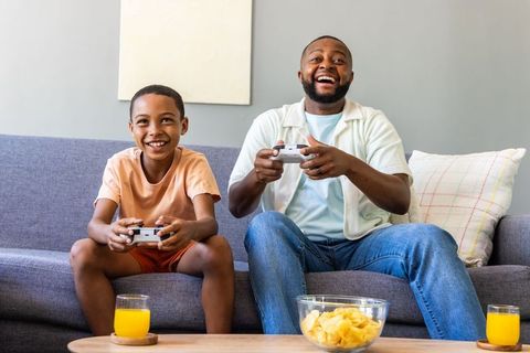 African american father and son playing video games on sofa laughing and relaxing