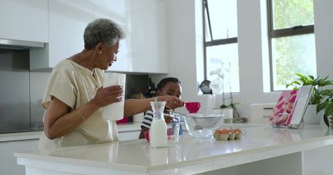 Grandparent and child preparing batter together in bright kitchen, multigenerational cooking
