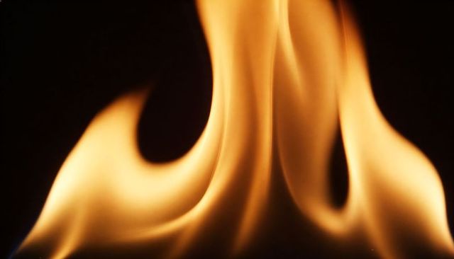 Dancing amber flames forming sculptural plume and arcs on black background golden glow