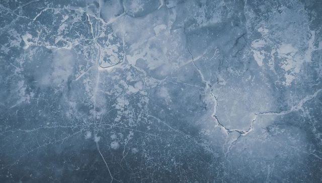 Revealing fractured blue-gray ice pattern from above with thin white veins and pockmarks