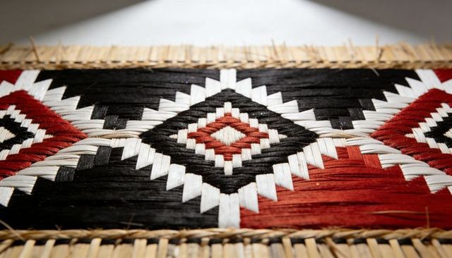 Handwoven geometric mat featuring black, white and red diamond motif with straw border