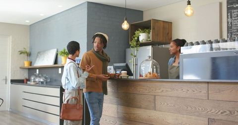 Young couple ordering coffee and chatting with barista at modern cafe counter