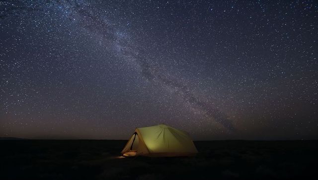 Glowing solo tent under milky way stretching across pristine desert night sky