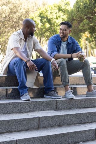 Two men sitting and chatting on stone steps in sunlit urban park