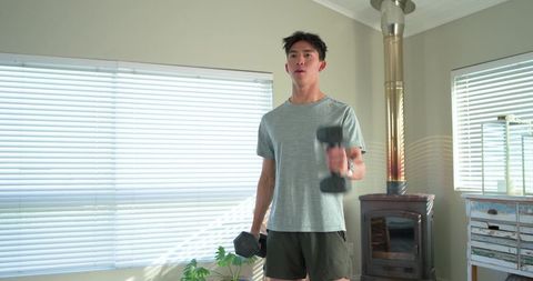 Asian man working out at home lifting hex dumbbells in bright modern living room