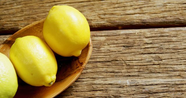 Three fresh lemons on a wooden plate against a rustic wooden background. Great for use in marketing materials related to healthy eating, organic produce, and natural food products. Perfect for posters, recipe books, websites, and food blogs emphasizing fresh and organic fruit.