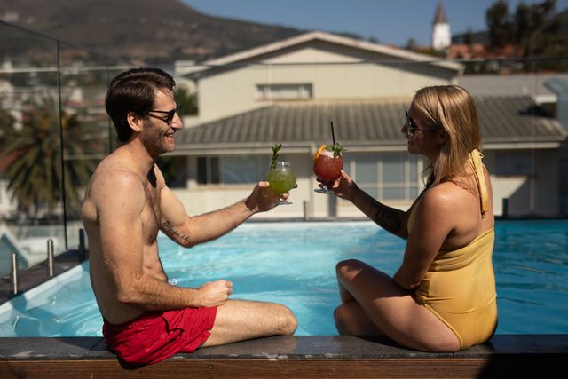 Side view close up of a Caucasian couple enjoying time off in summer at a hotel, relaxing by a private pool, drinking fruity cocktails, smiling and talking.