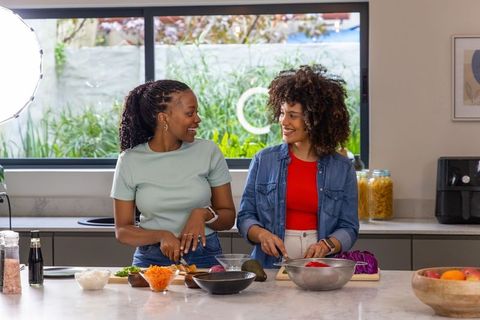 Two african american women preparing healthy meal together in bright modern kitchen