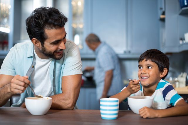Father and son sharing a joyful breakfast moment in a modern kitchen. Ideal for use in family-oriented advertisements, parenting blogs, lifestyle articles, and promotional materials highlighting family values and morning routines.
