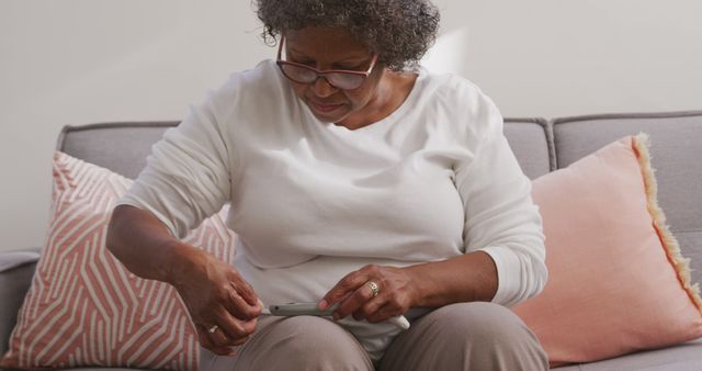 Senior african american woman sitting on sofa and testing blood sugar level. Senior lifestyle, free time, healthcare and domestic life.